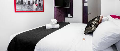 Une chambre d’hôtel moderne équipée d’un lit, d’un téléviseur à écran plat, d’une armoire et d’un tableau encadré au mur.