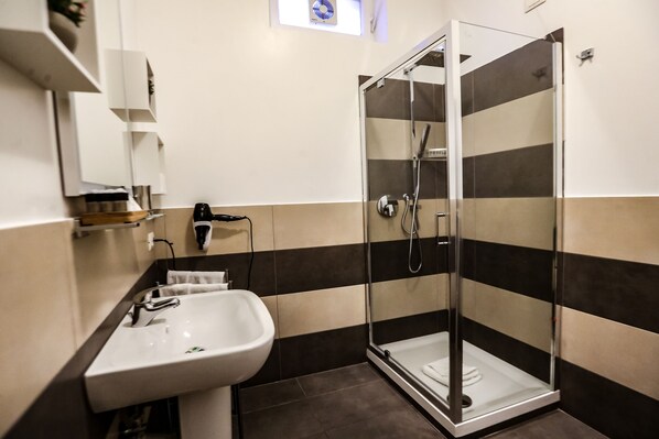 Un baño moderno con ducha de vidrio, un lavamanos blanco y un perchero para toallas.