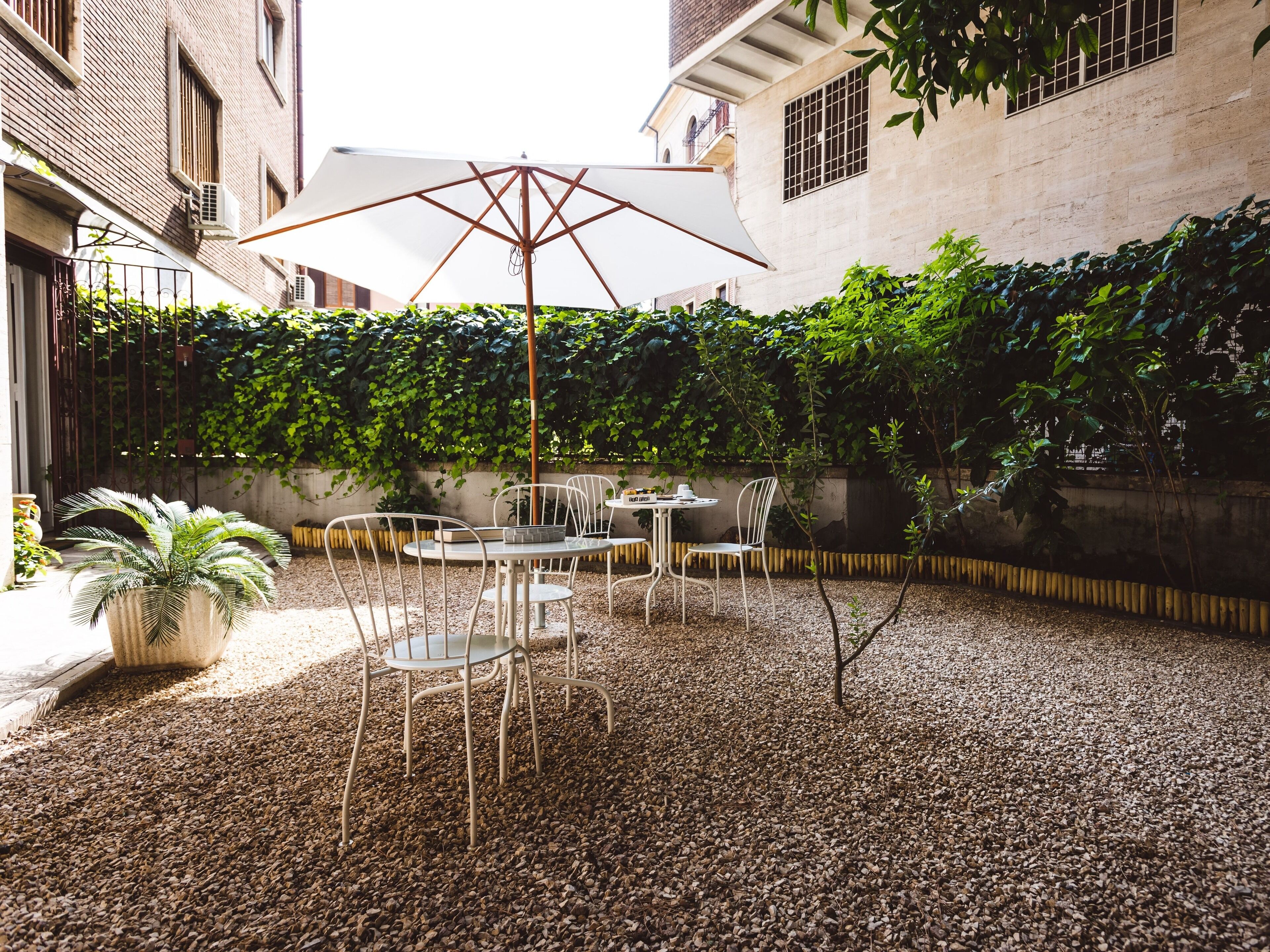 Un patio al aire libre con una mesa y sillas, rodeado de grava y un seto.