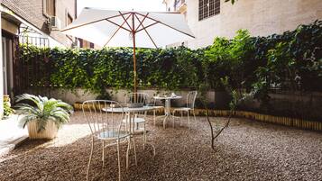 Un patio al aire libre con una mesa y sillas, rodeado de grava y un seto.