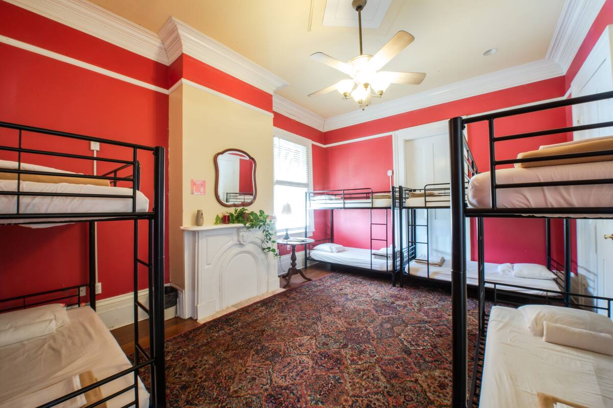 A dormitory room with bunk beds, a ceiling fan, a mirror, and a patterned carpet.