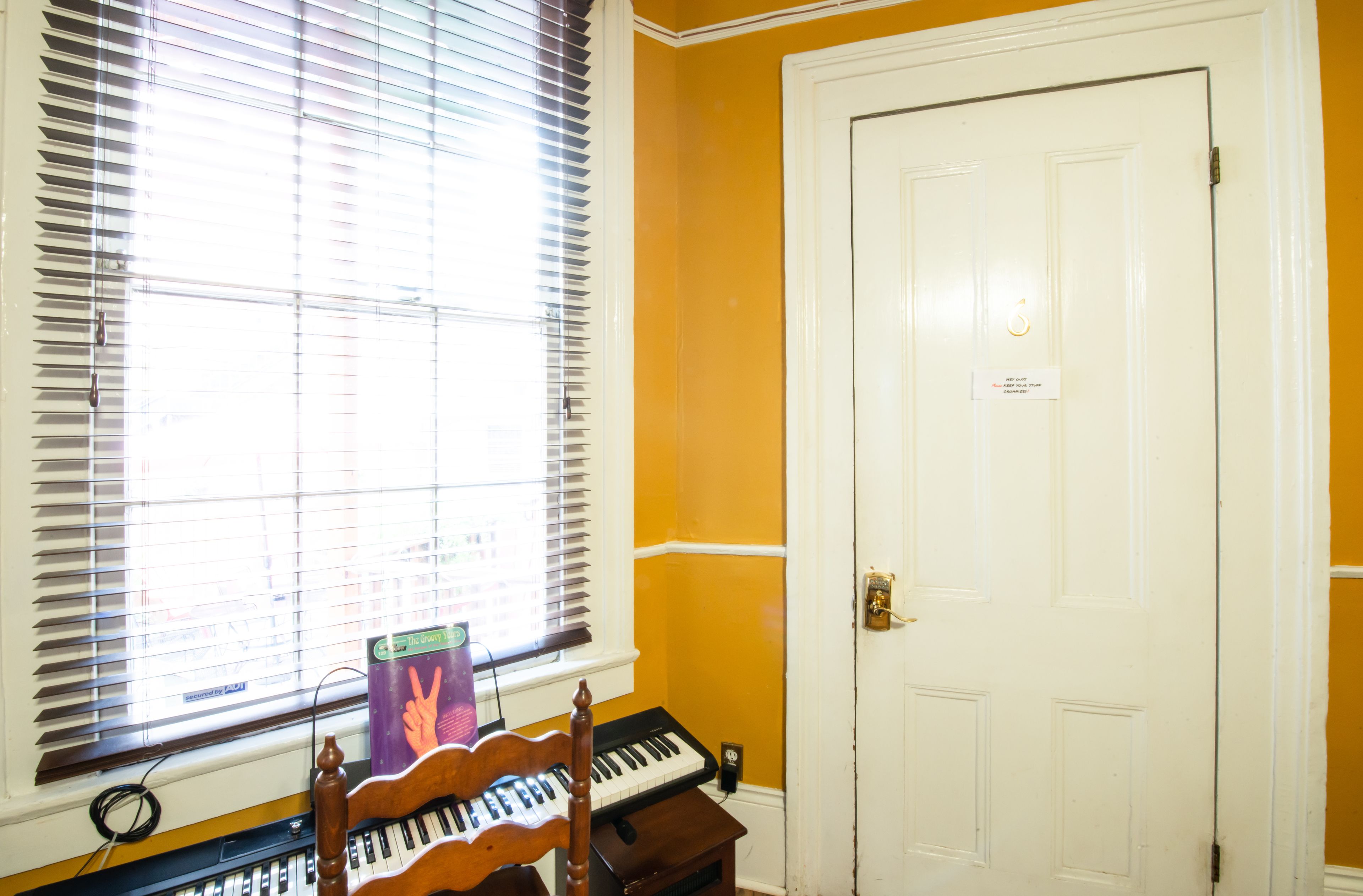 A room with a piano, a window with blinds, and a white door.
