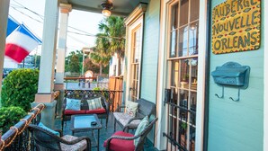 Un patio al aire libre con mobiliario de mimbre, una bandera francesa y un letrero que dice "Auberge Nouvelle Orleans".