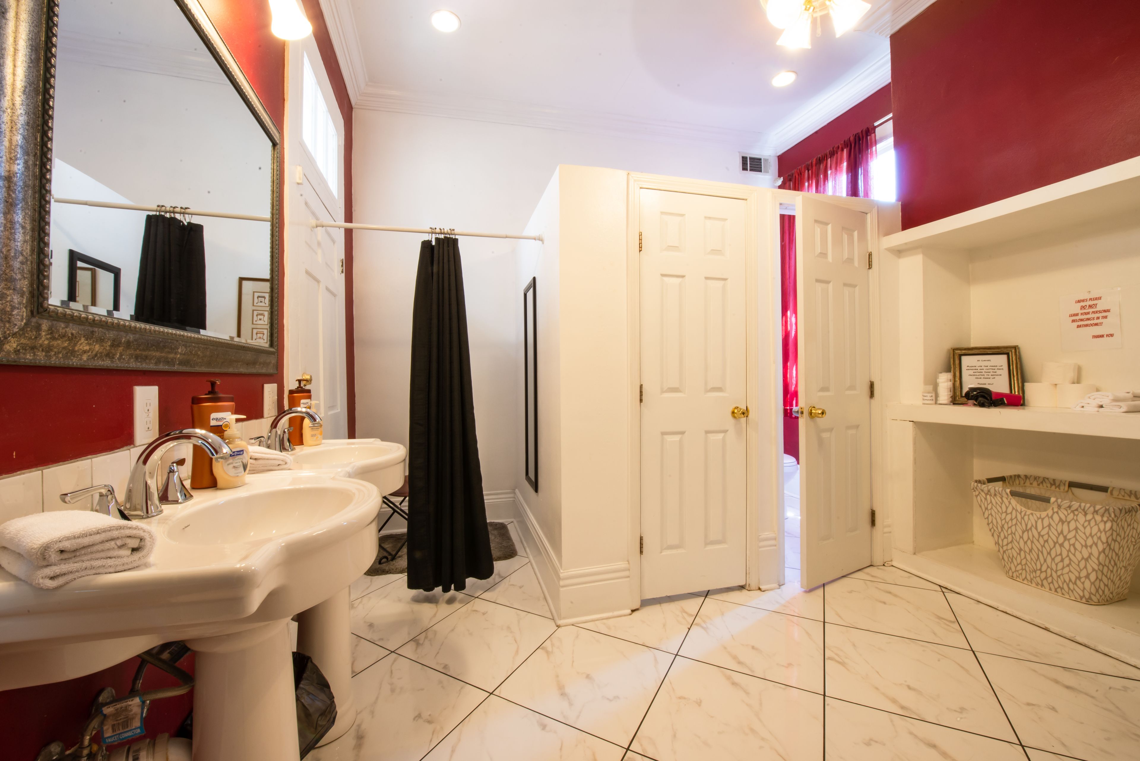 Un baño con lavamanos blanco, espejo y puerta que da a otra habitación.