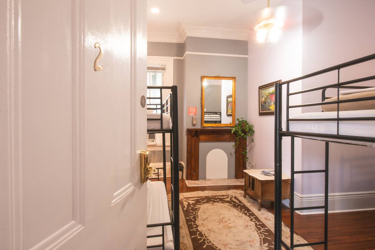 A hallway with a wooden floor, a white door, a black metal gate, a mirror, and a small table with a plant.
