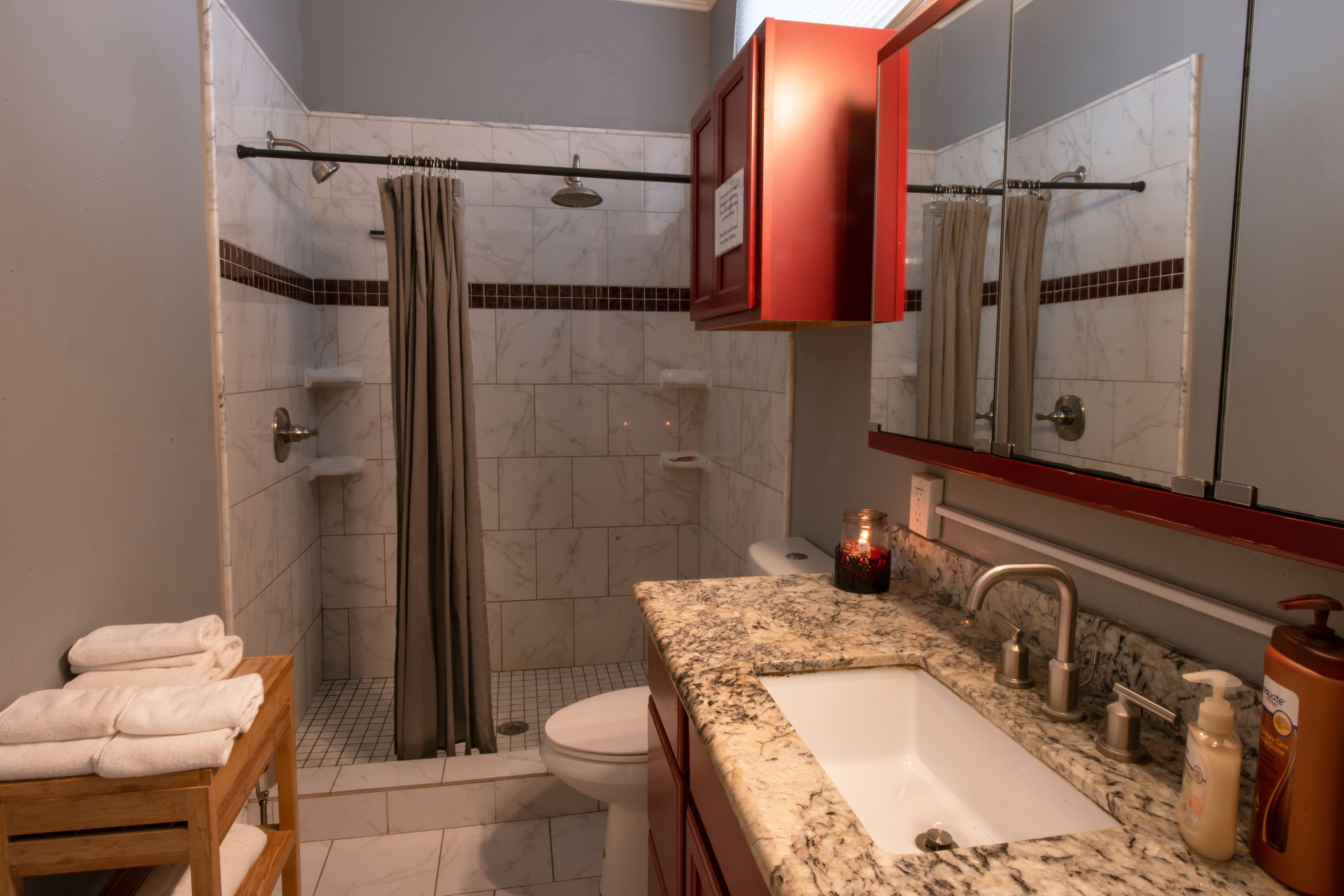 Une salle de bain équipée d’une douche, de toilettes, d’un lavabo et d’une étagère en bois où sont rangées les serviettes.