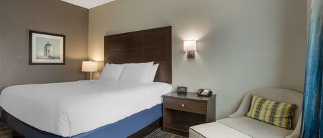 A hotel room with a large bed, a nightstand with a lamp, a chair, and a small table.