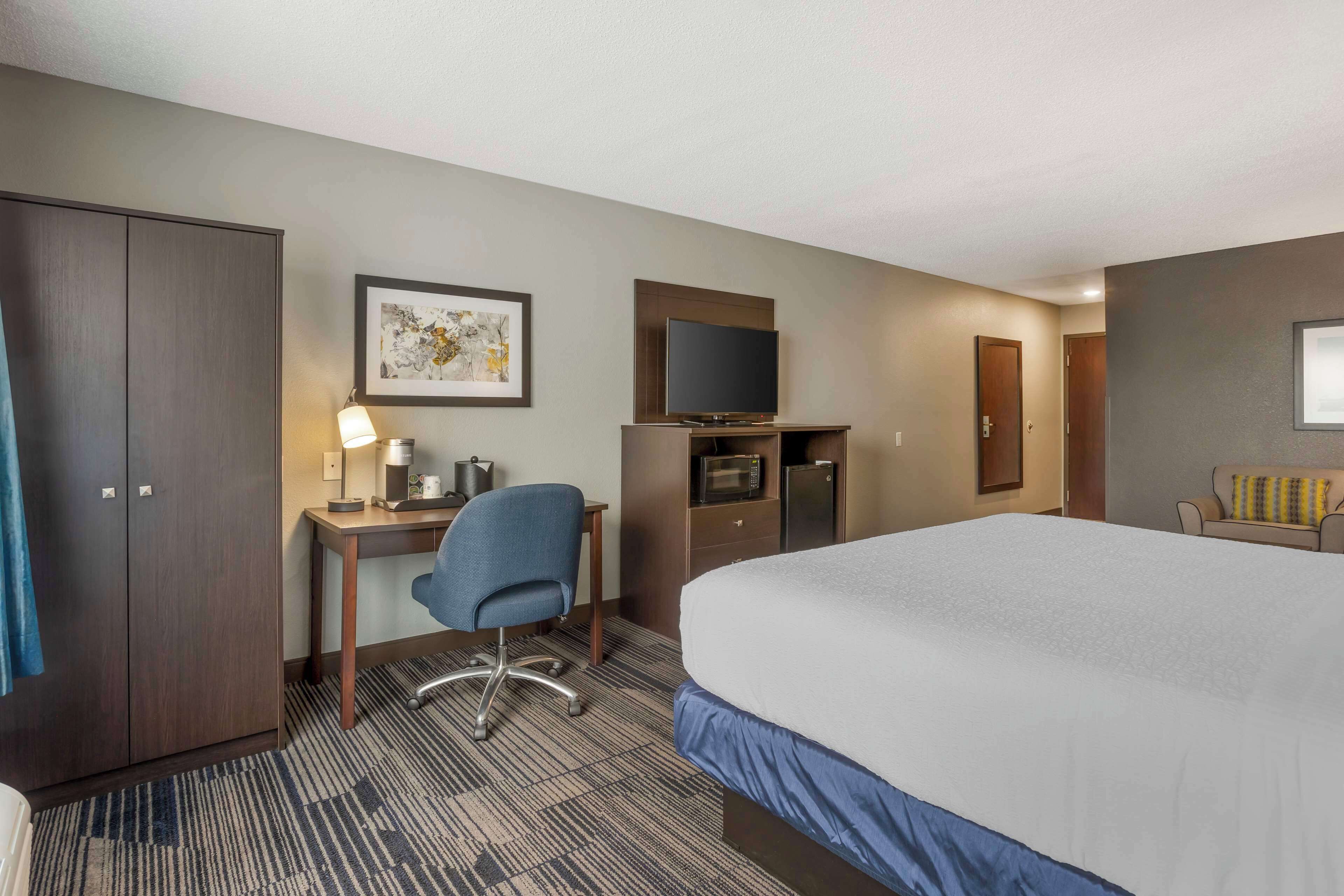 A hotel room with a large bed, a desk with a chair, a television, a microwave, and a wardrobe.