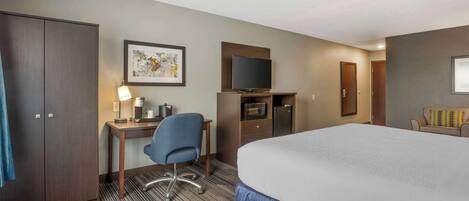 A hotel room with a large bed, a desk with a chair, a television, a microwave, and a wardrobe.