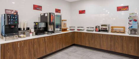 A self-service breakfast area with coffee machines, a yogurt dispenser, and a refrigerated display.