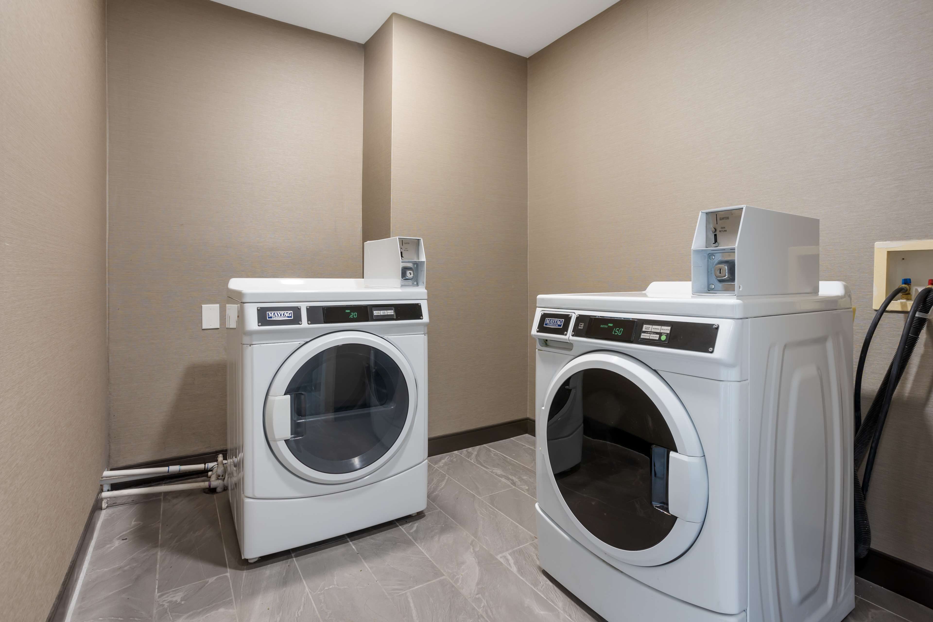 Two front-loading washing machines in a laundry room with beige walls and tiled flooring.