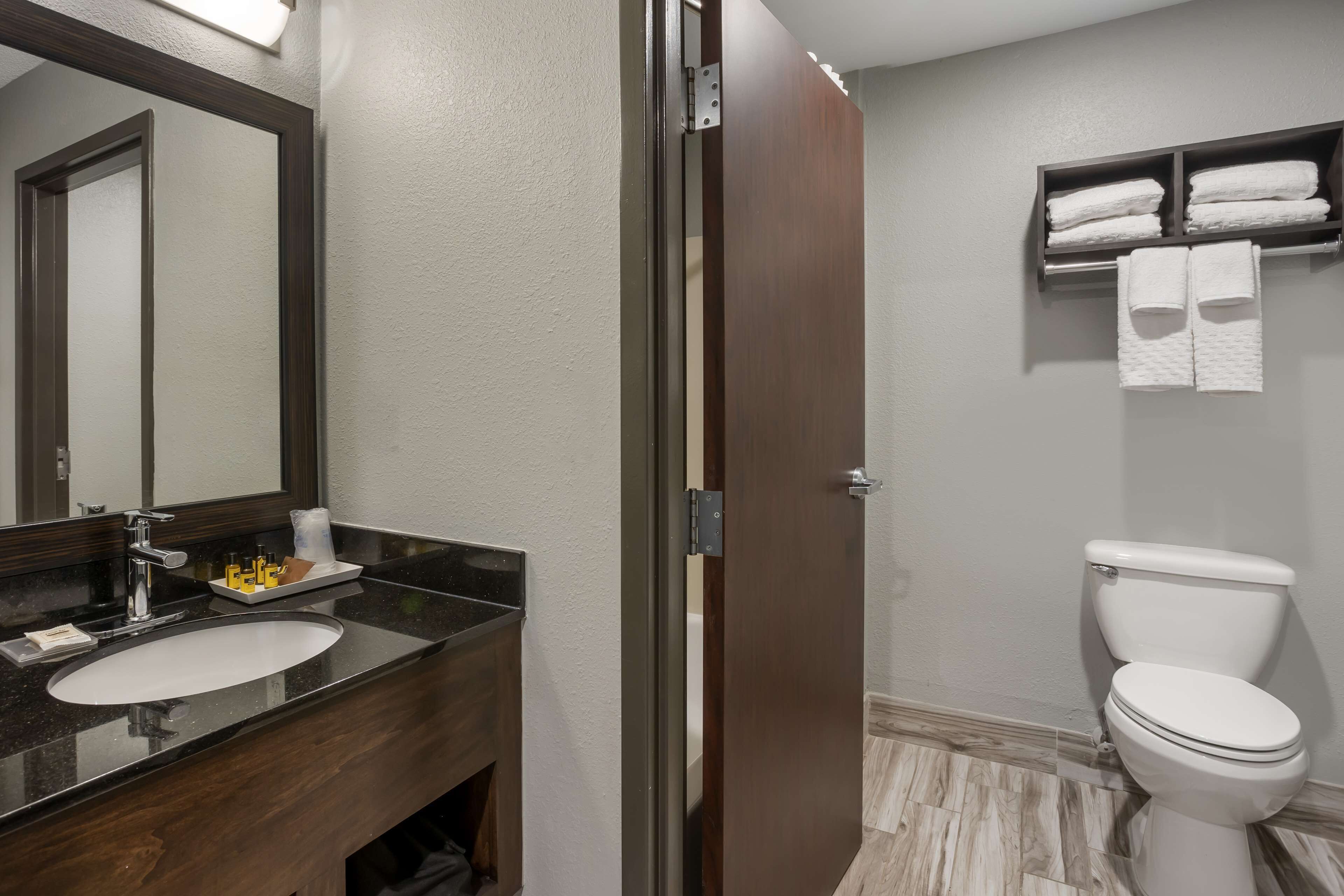 Une salle de bain avec un meuble-lavabo en bois foncé, un lavabo blanc, un miroir, des toilettes et un porte-serviettes avec des serviettes.