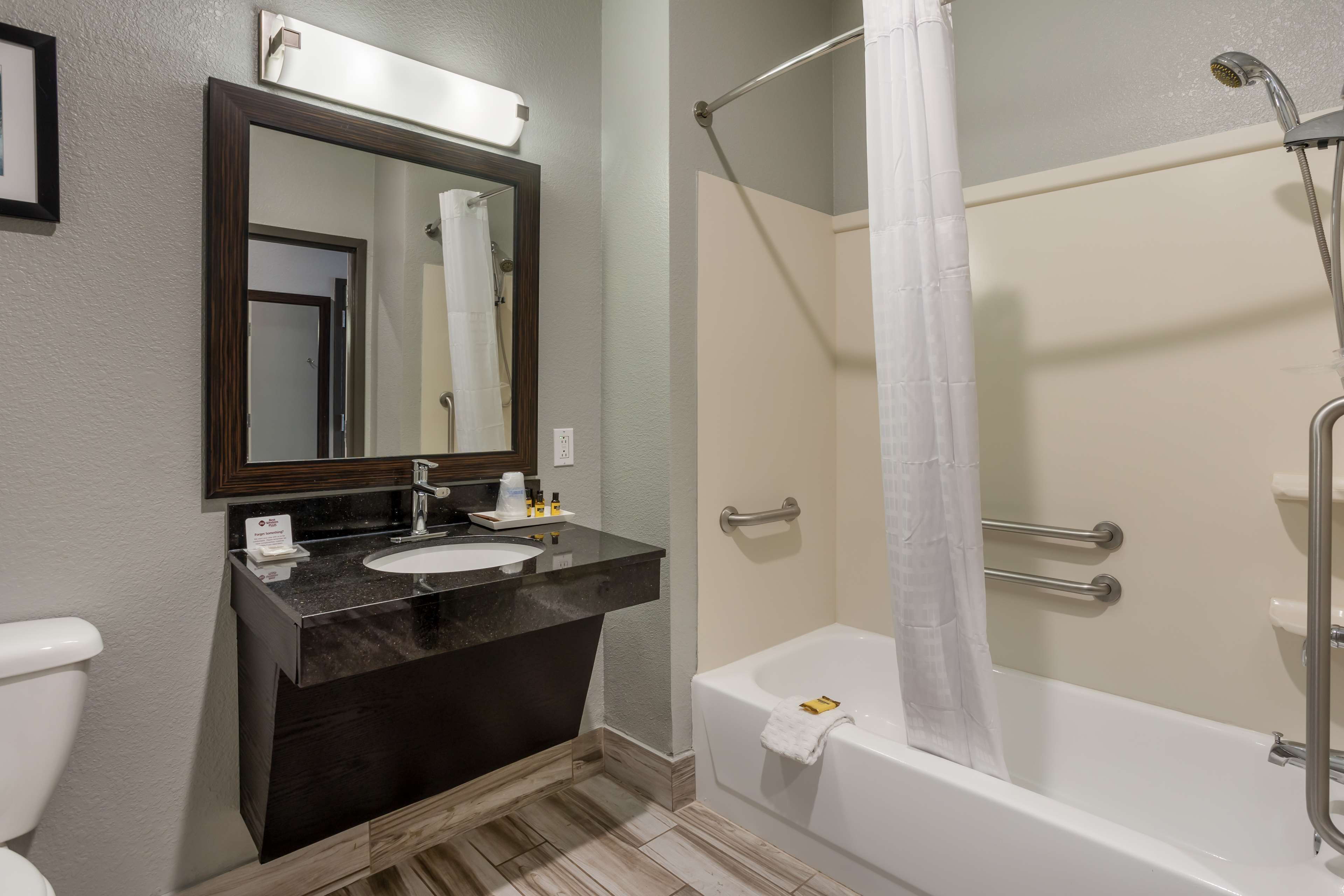 A bathroom with a dark marble vanity, a white sink, a mirror, a shower with a glass door, and a white toilet.