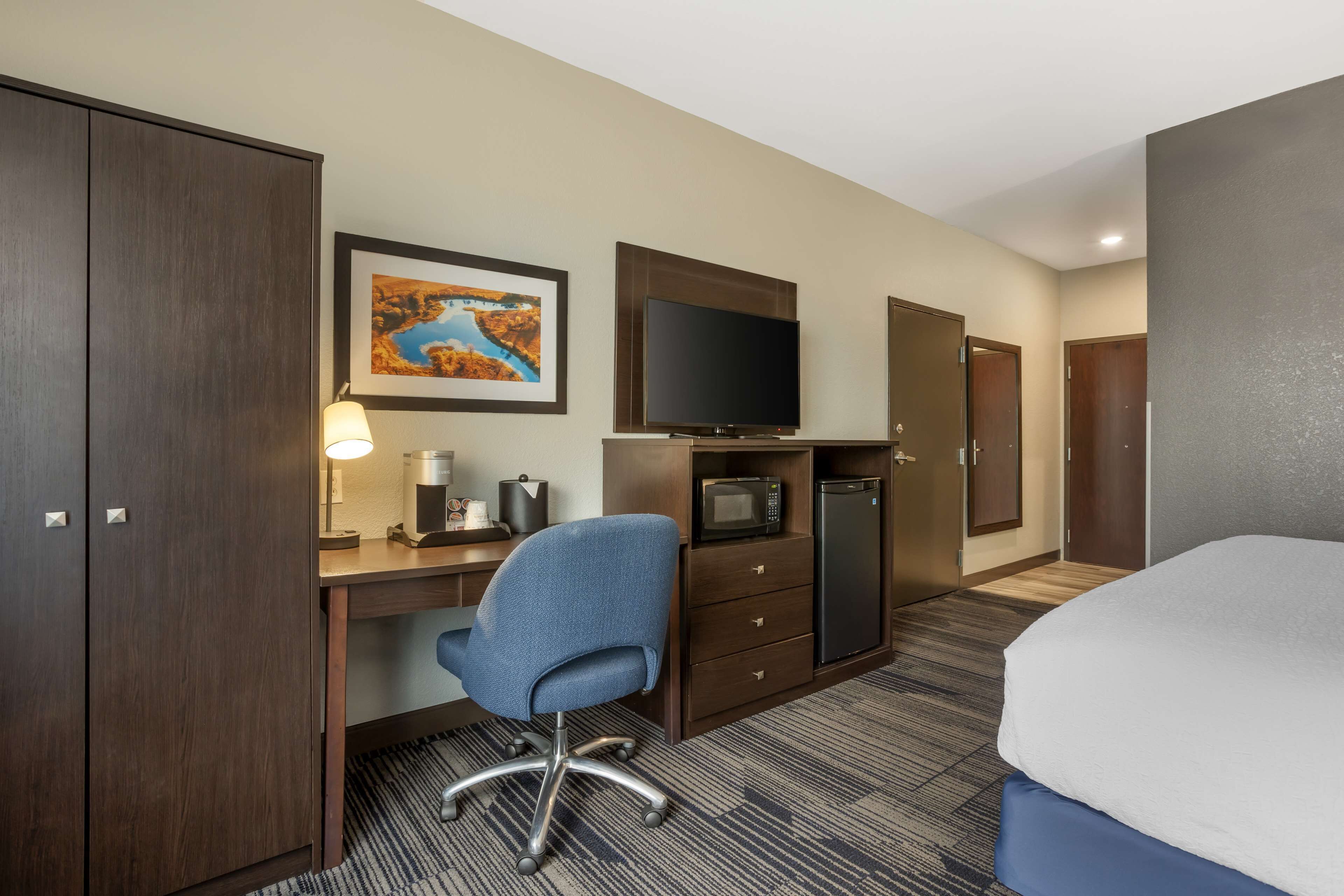 A hotel room with a bed, a desk with a chair, a television, a microwave, a refrigerator, and a cabinet.