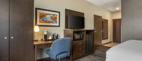Habitación de hotel con cama, escritorio con silla, televisión, microondas, refrigerador y mueble.