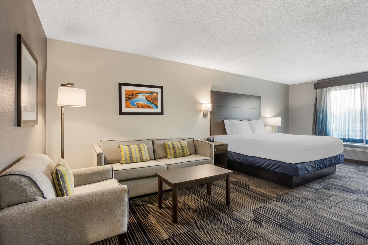 A hotel room with a bed, a sofa, a coffee table, and a painting on the wall.