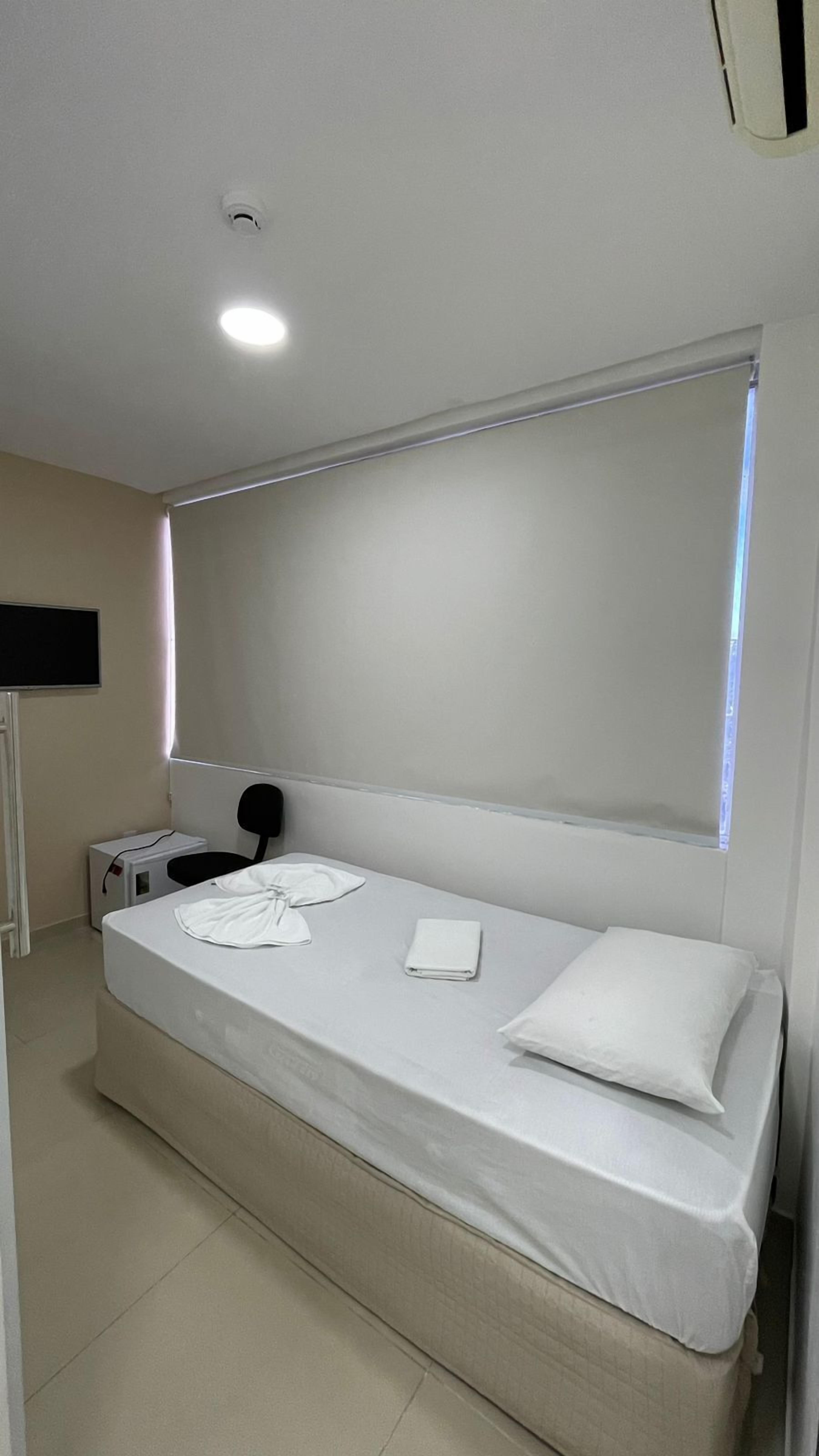 Habitación individual con una cama, un ventanal grande, televisión de pantalla plana y mesita de noche con lámpara.