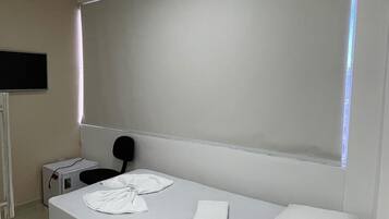 Habitación individual con una cama, un ventanal grande, televisión de pantalla plana y mesita de noche con lámpara.