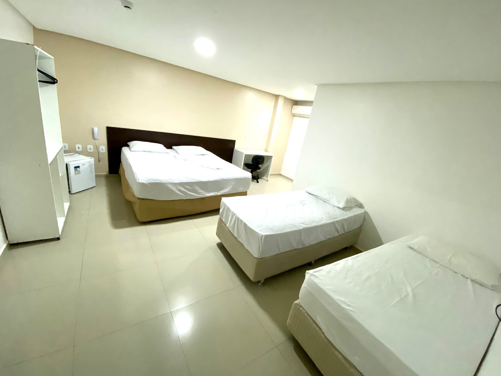 Habitación de hotel con dos camas, un escritorio, una silla, un armario y una mesita de noche.