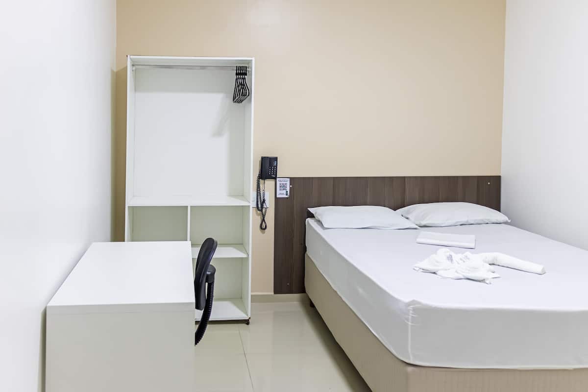 Une chambre d’hôtel avec un lit, un bureau blanc, un téléphone et une étagère.