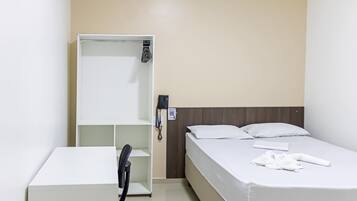 Una habitación de hotel con una cama, un escritorio blanco, un teléfono y una estantería.