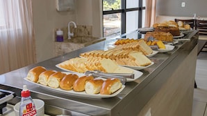 A buffet with various breads and rolls, a bottle of Adocyl, and a window with curtains.