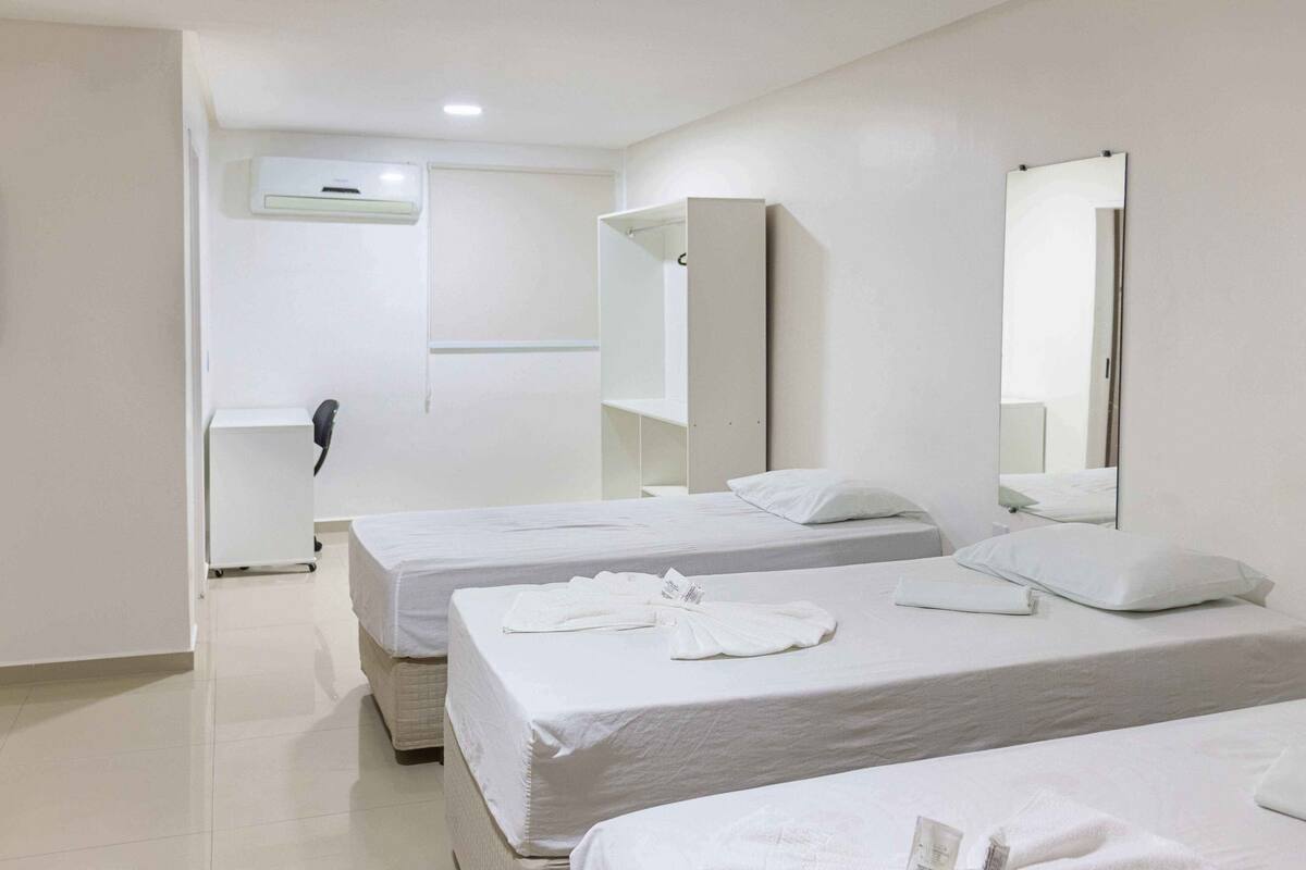 Une chambre d’hôtel avec deux lits, du linge de lit blanc, un grand miroir et un téléphone fixé au mur.