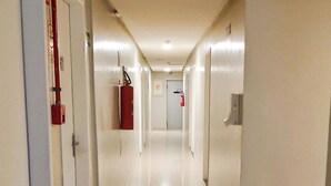 A long, well-lit hallway with doors on both sides, a fire extinguisher mounted on the wall, and a fire alarm visible in the distance.