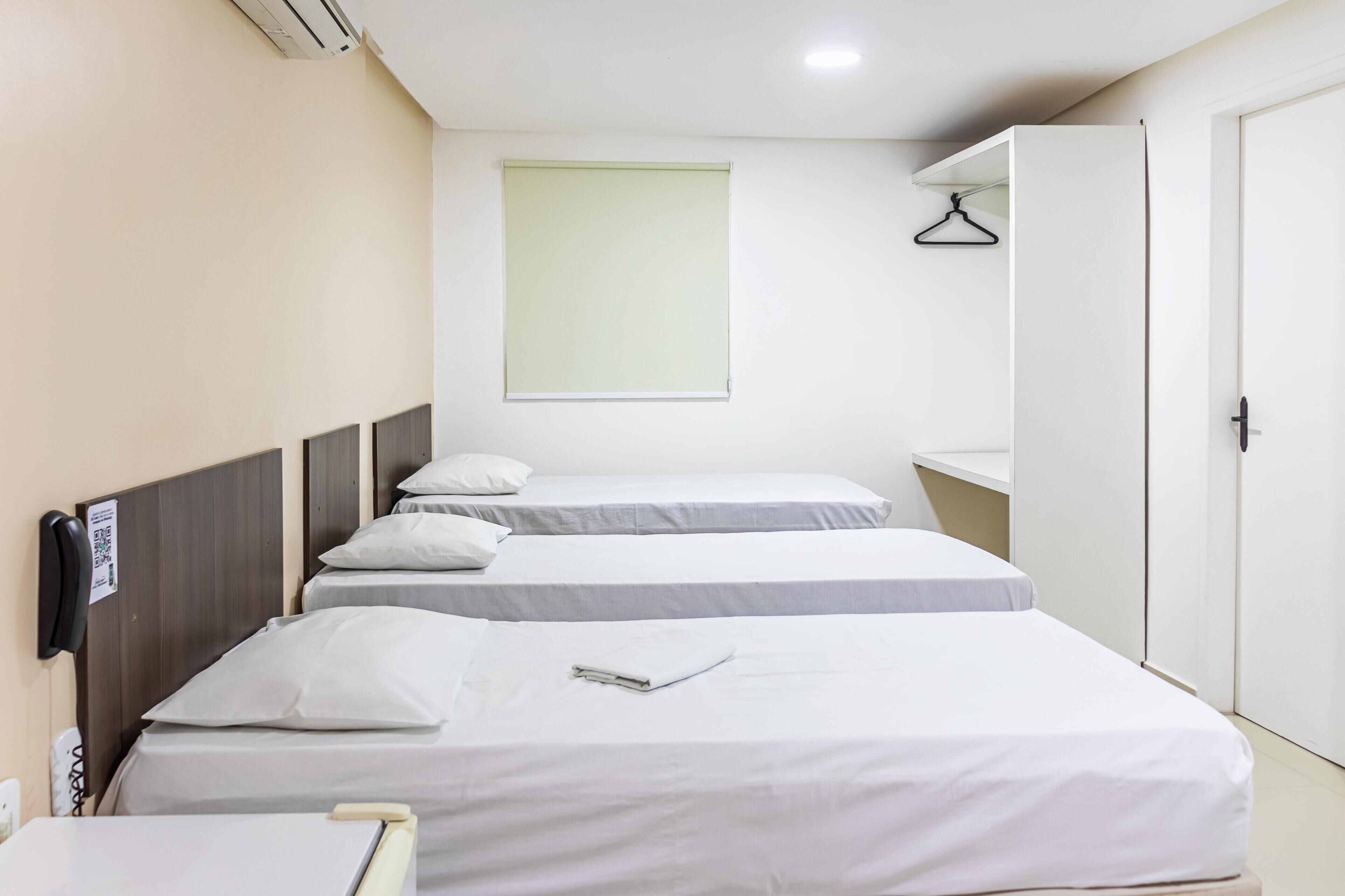 A hotel room with two single beds, a wardrobe, a bedside table, and a hanging coat rack.