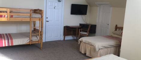 A dormitory room with bunk beds, a desk, a chair, and a TV.