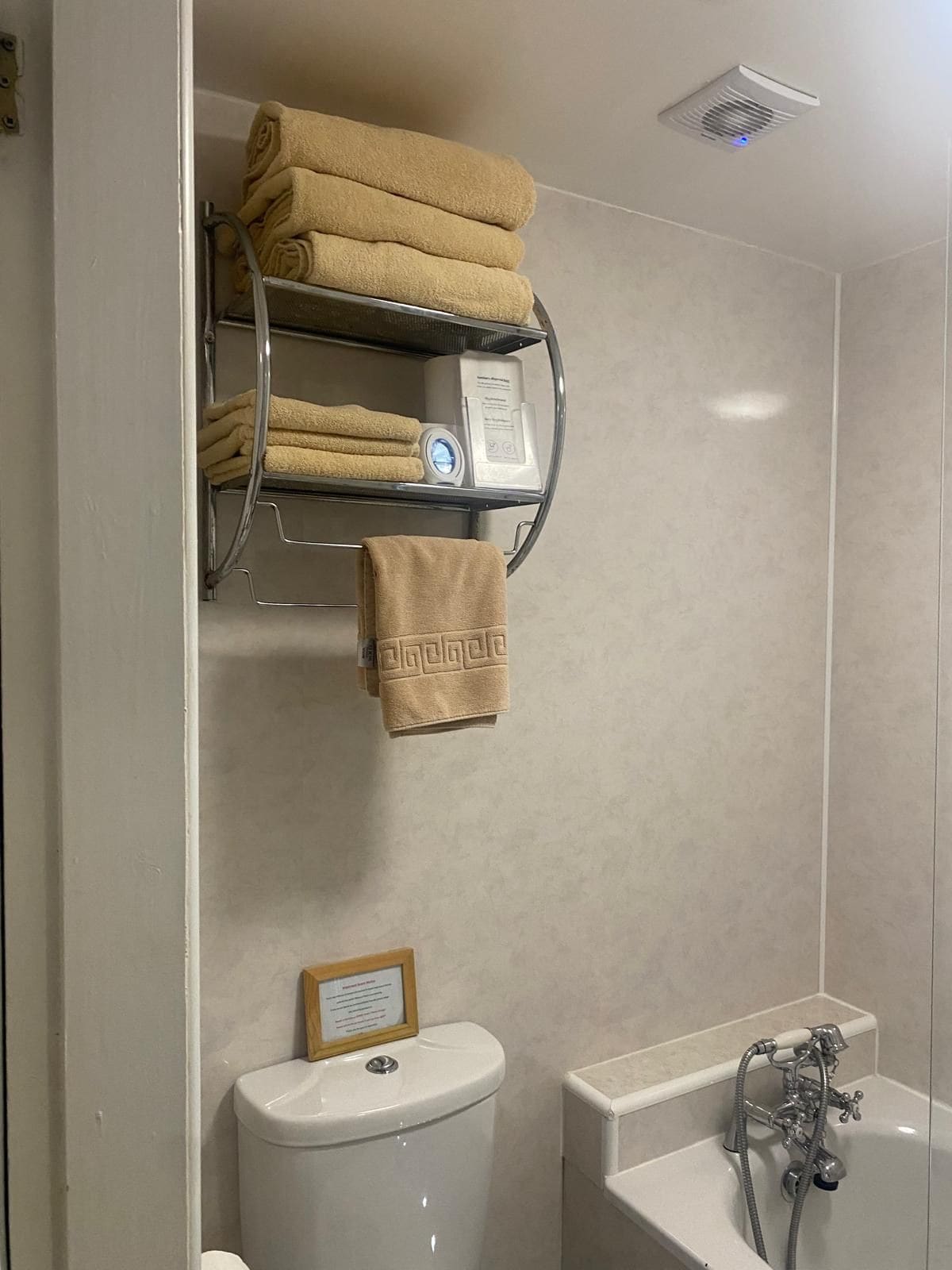A bathroom with a toilet, a sink, a bathtub, a towel rack with folded towels, and a showerhead.