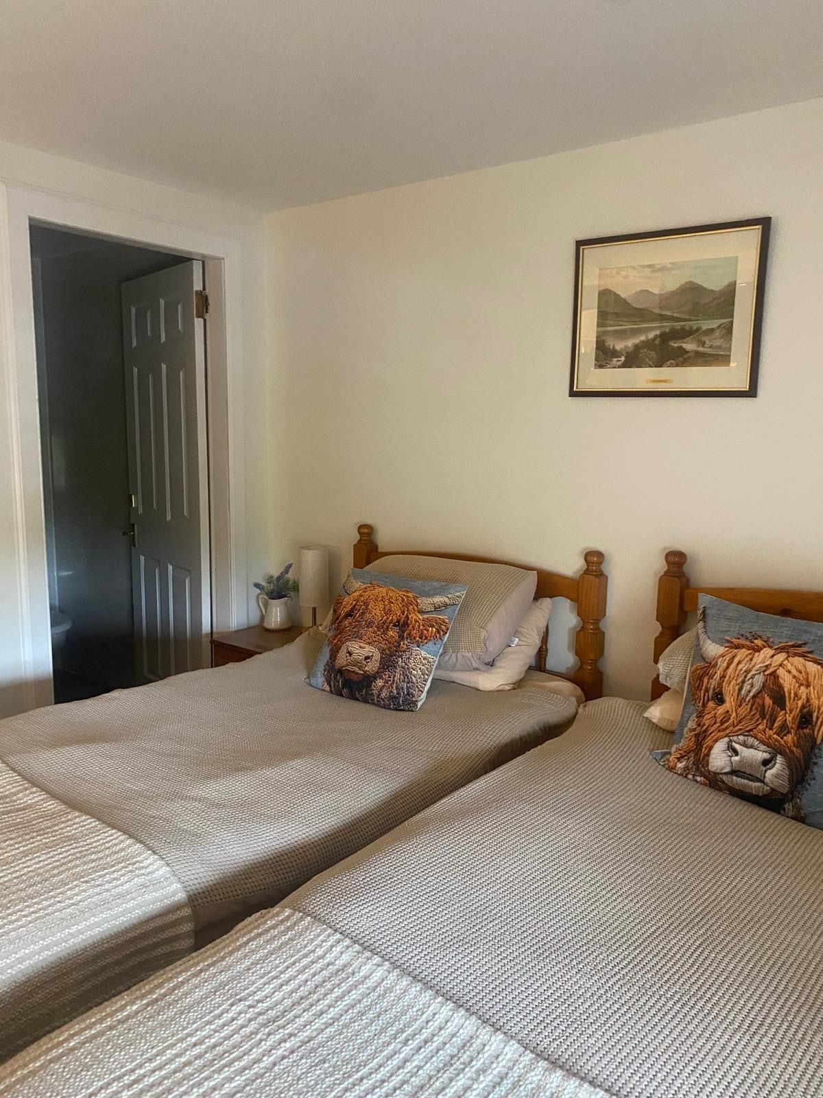 A bedroom with two beds, a wooden headboard, a framed landscape picture, and a door leading to another room.