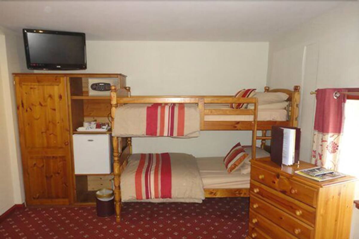Quarto com beliche, televisão acima da cama inferior, cômoda de madeira e uma pequena escrivaninha com cadeira.