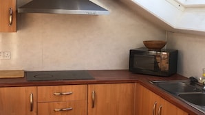 A compact kitchen with wooden cabinets, a built-in microwave, and a skylight.