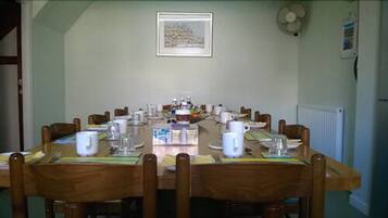 A dining room with a long table set for a meal, chairs, a fan, and a framed picture on the wall.