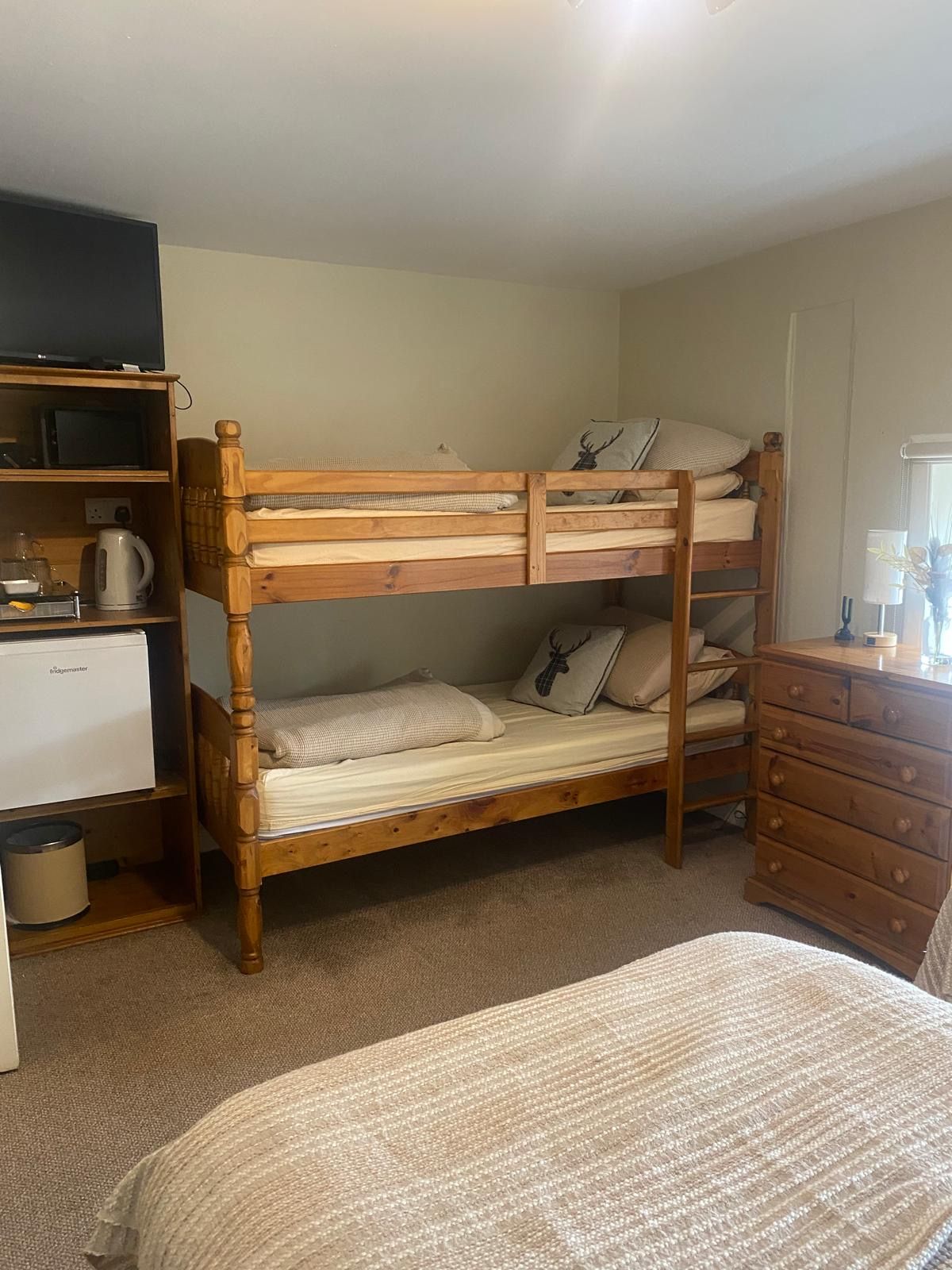 A bunk bed with a wooden frame, a small desk with a kettle, and a dresser with drawers.