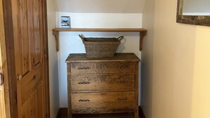 Une commode en bois avec des tiroirs et un panier posé sur le dessus, une porte en bois et un miroir accroché au mur.