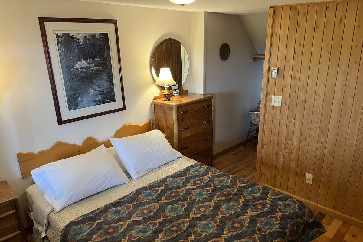 A bedroom with a bed, a dresser, a mirror, and a framed picture on the wall.