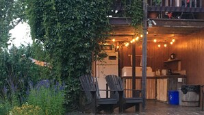 Un espace extérieur aménagé avec des chaises et une table en bois, entouré de verdure et illuminé de guirlandes lumineuses.