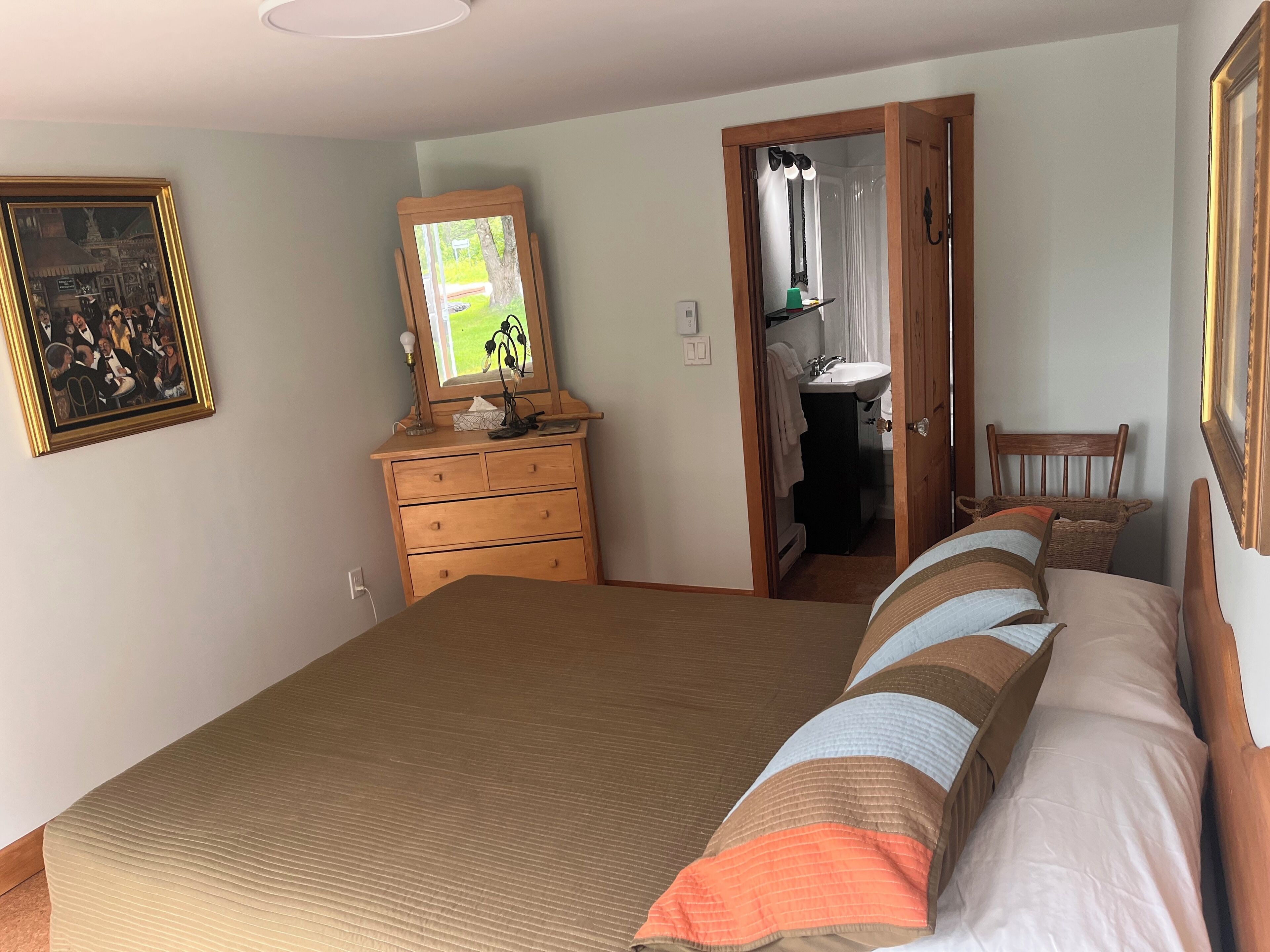 Una camera da letto con un letto grande, una cassettiera in legno, uno specchio e una porta che dà su un bagno.