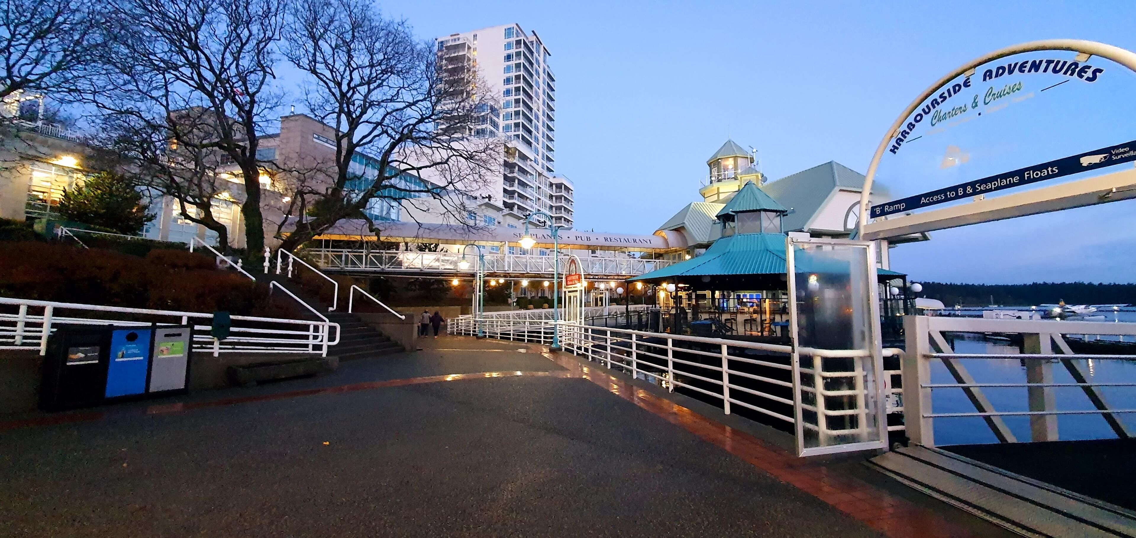 A waterfront promenade with a bridge leading to a restaurant and a sign for 'Warriorside Adventures'.
