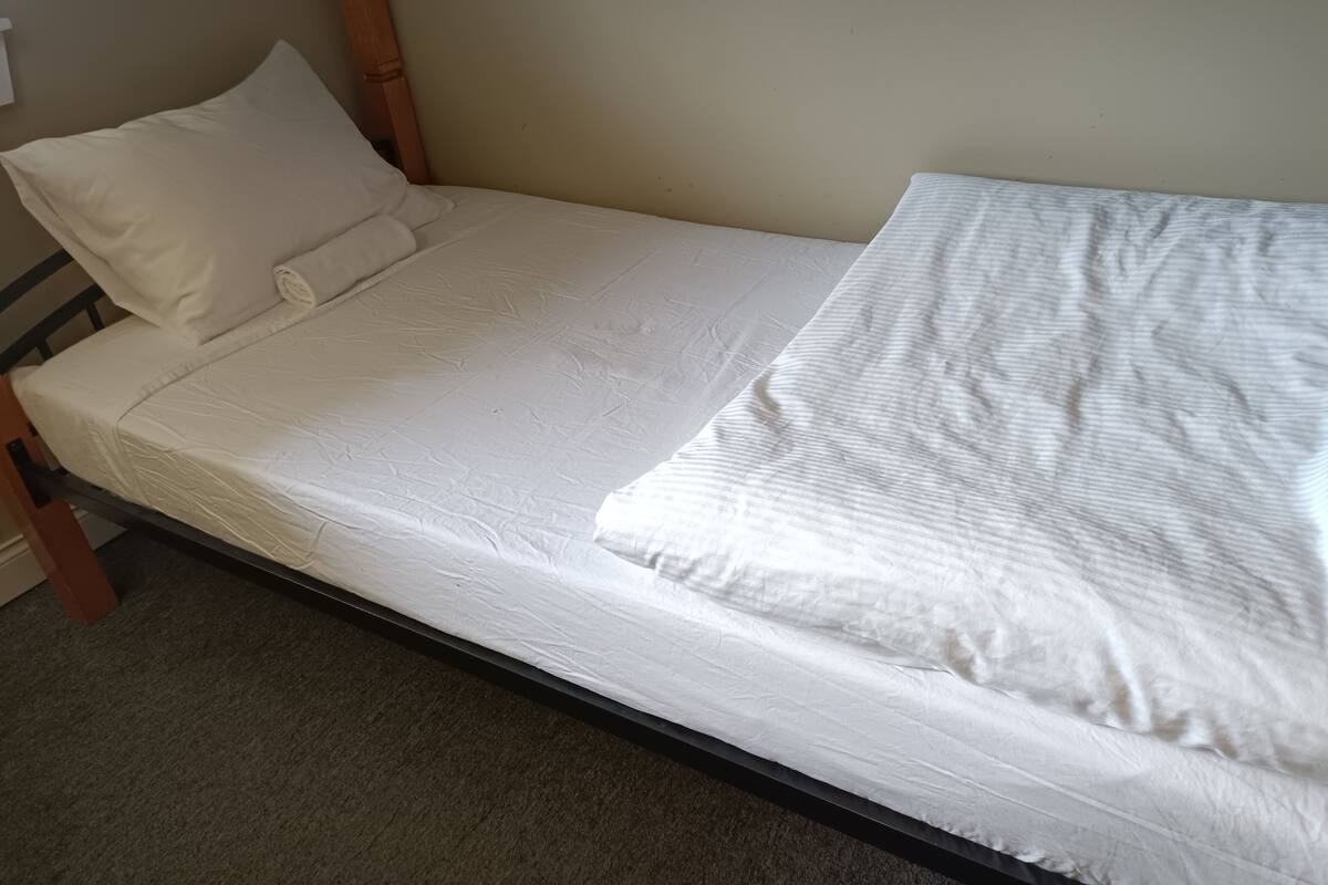 Una cama individual con estructura de madera, ropa de cama blanca y una pared lisa.