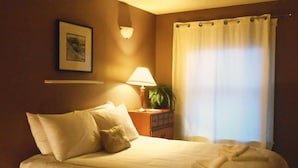 Ein ordentlich gemachtes Bett mit Kissen, einer Nachttischlampe, einer kleinen Pflanze und einem Fenster mit Vorhängen.