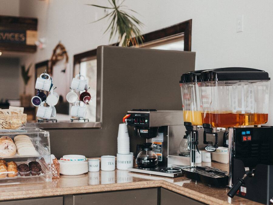 Un comptoir de café avec une machine à café, un distributeur de thé et un présentoir de pâtisseries et de biscuits.