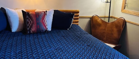 Un dormitorio con una cama grande, cabecera, lámpara de pared y una lámpara de pie, además de una ventana con persianas.