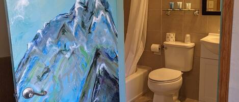 A bathroom with a toilet, shower, and a painting of a mountain landscape on the wall.