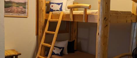 A bunk bed room with a ladder, a small table, and a framed picture on the wall.
