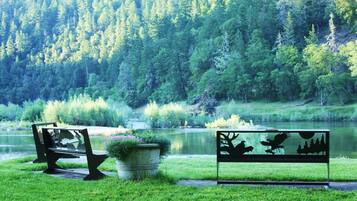 A bench and a metal sign with wildlife silhouettes by a lake surrounded by trees.