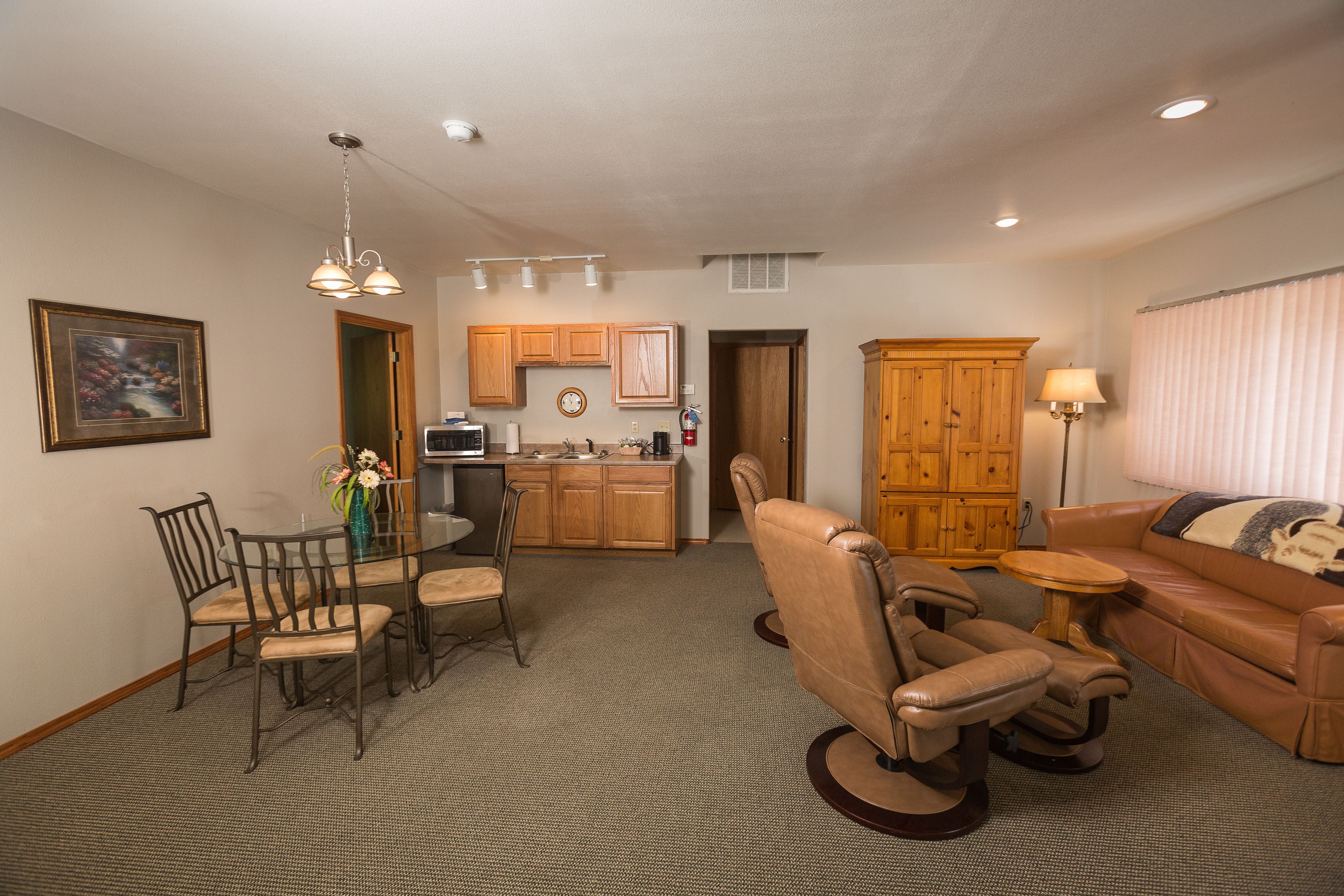 A spacious living room with a leather sofa, a dining area with a glass table, and a kitchen area with wooden cabinets and a microwave.