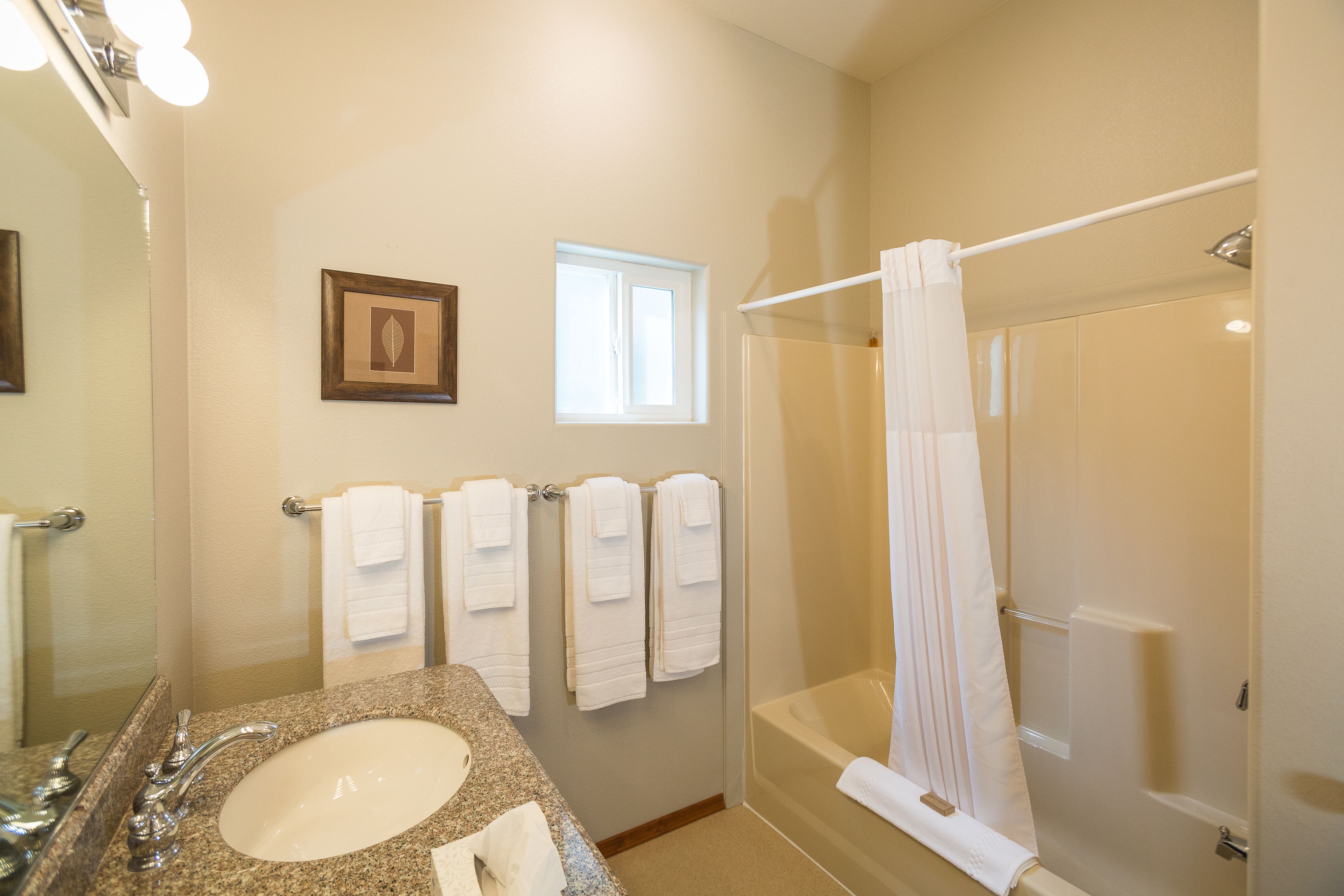 A bathroom with a granite sink, a large mirror, a framed picture on the wall, a window, and a glass-enclosed shower area.